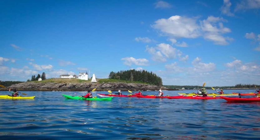 Colorful kayaks are paddled by students on calm blue water near a small island